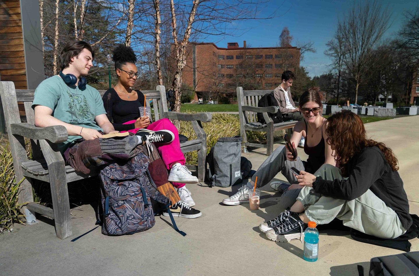 four students gathered, two on a bench, two sitting on the sidewalk