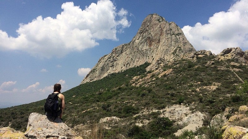 student sitting in rocky meadow looking at outcropping