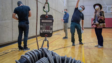 Students and professors stand int he gym preparing to climb 