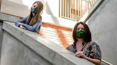 two students who won an award posing together in masks on a staircase