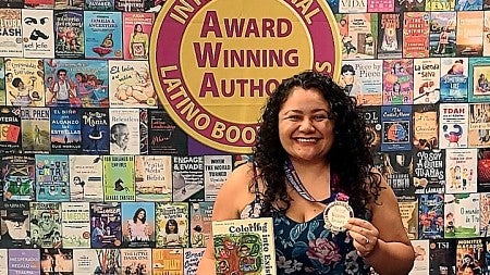 Isabel Millán stands in front of a poster of book covers holding her book