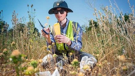 a student wearing a reflective jacket and a hat in the middle a of a flower bed