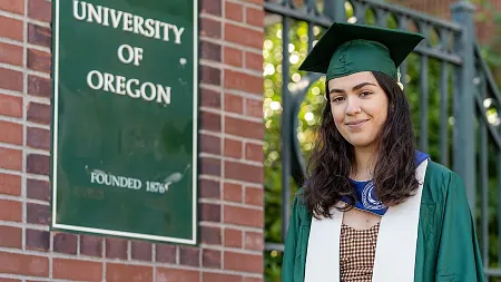 a person wearing a cap and gown by dad's gate at the UO campus