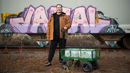woman standing in front of a street mural with a wagon full of supplies