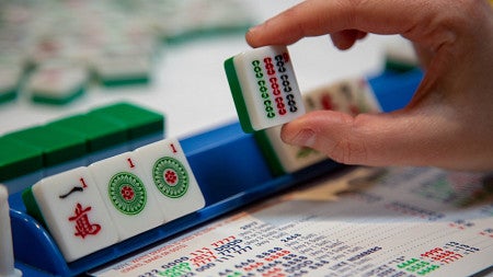 hand holding a mahjong tile with other tiles on the table below it