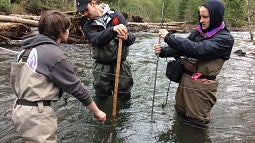 Three students studying the river with waders on. 