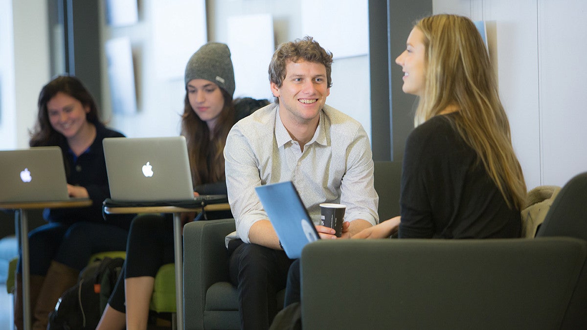 male and female student talking with laptops in lounge area