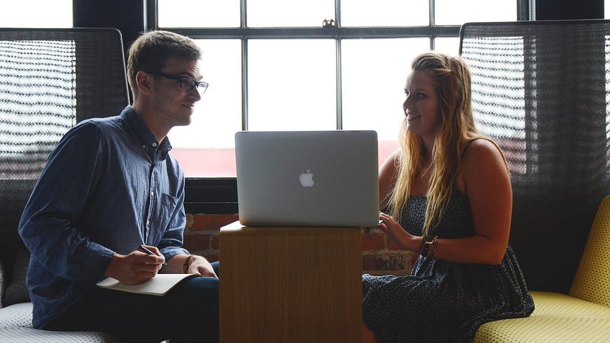 man and woman sitting across the table from one another with laptop