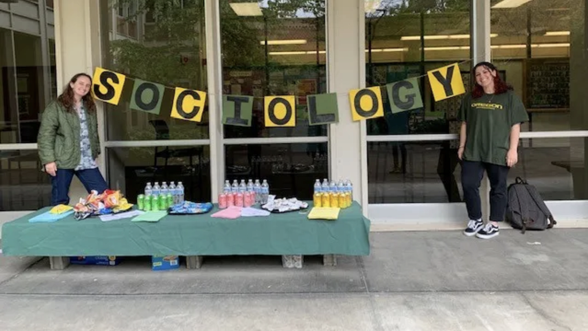 students outside at table event with hand-made Sociology sign