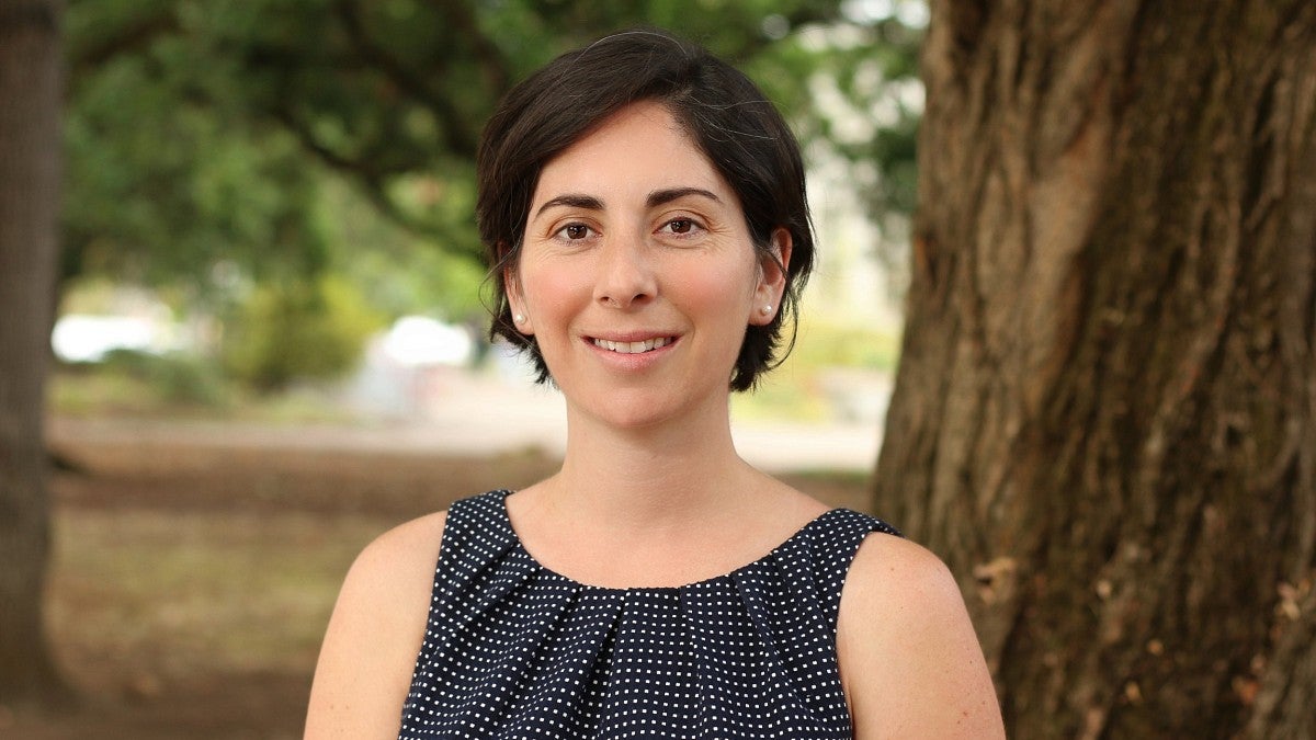 a woman with short dark hair smiling in front of a tree