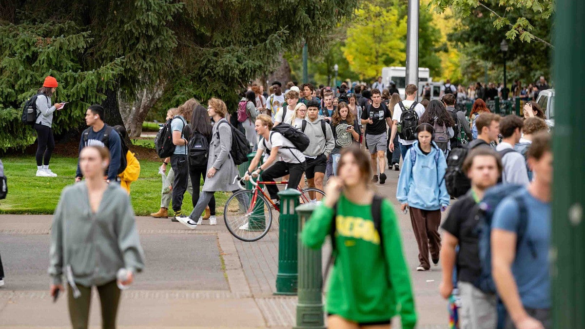 a crowd of students walking to class, the camera is focused on a student riding on a bicycle without a helmet