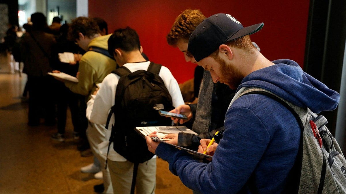 A person in a group of students taking notes in a hallway