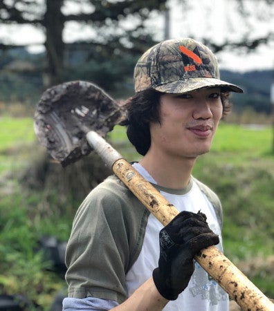 ELP student shouldering shovel with muddy gloves