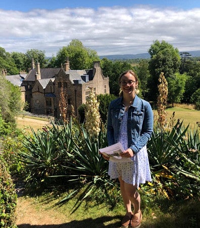 Michele Pflug standing with landscape of plants and old building behind her