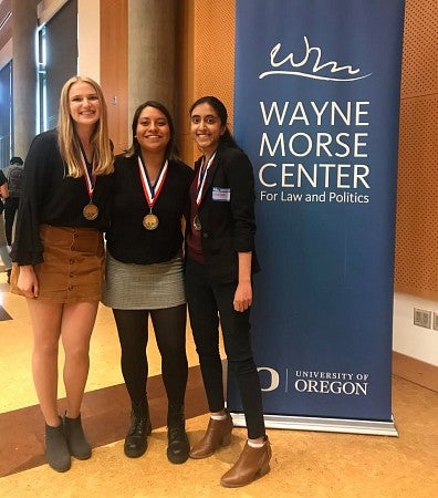 three women stand beside a blue banner that says Wayne Morse Center