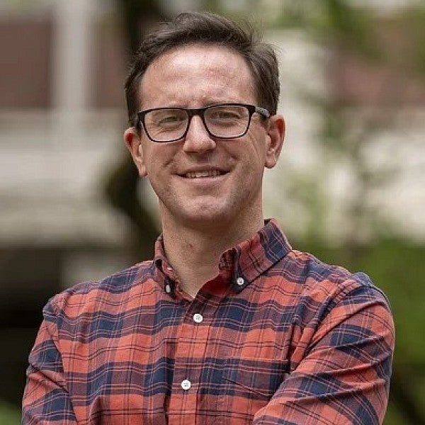 Political Science faculty member Neil O'Brien stands outside smiling with arms crossed