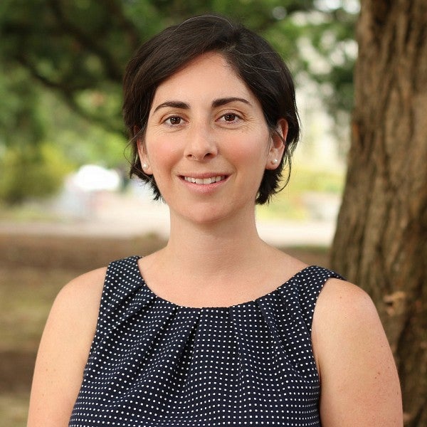 a woman with short dark hair smiling in front of a tree