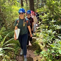 Students in hard hats walking through the forest in single file.