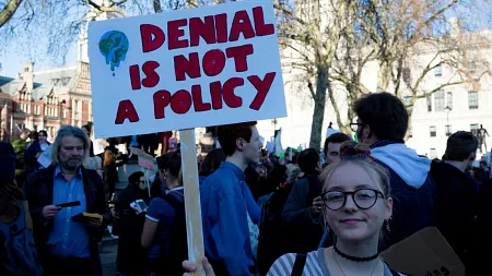 young person at climate rally holding sign reading "denial is not a policy" with illustration of melting planet