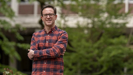 Political Science faculty member Neil O'Brien stands outside smiling with arms crossed
