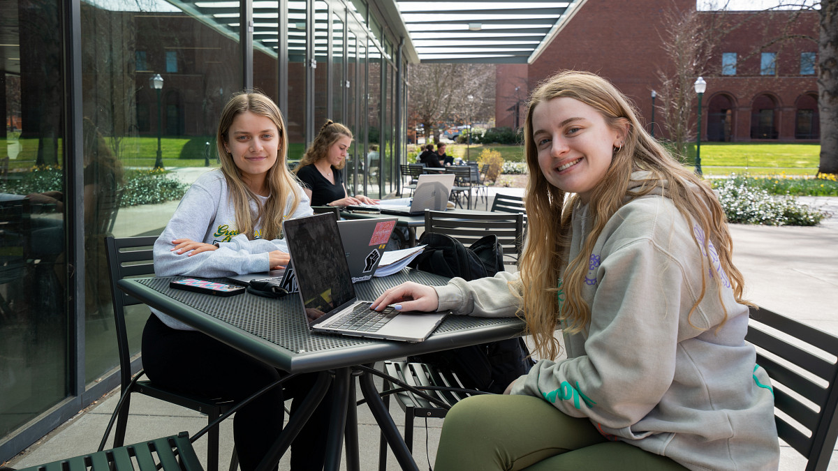two students sitting at a picnic table with laptops
