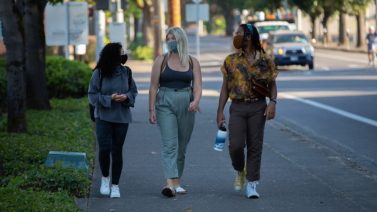 three students wearing face masks and walking on sidewalk