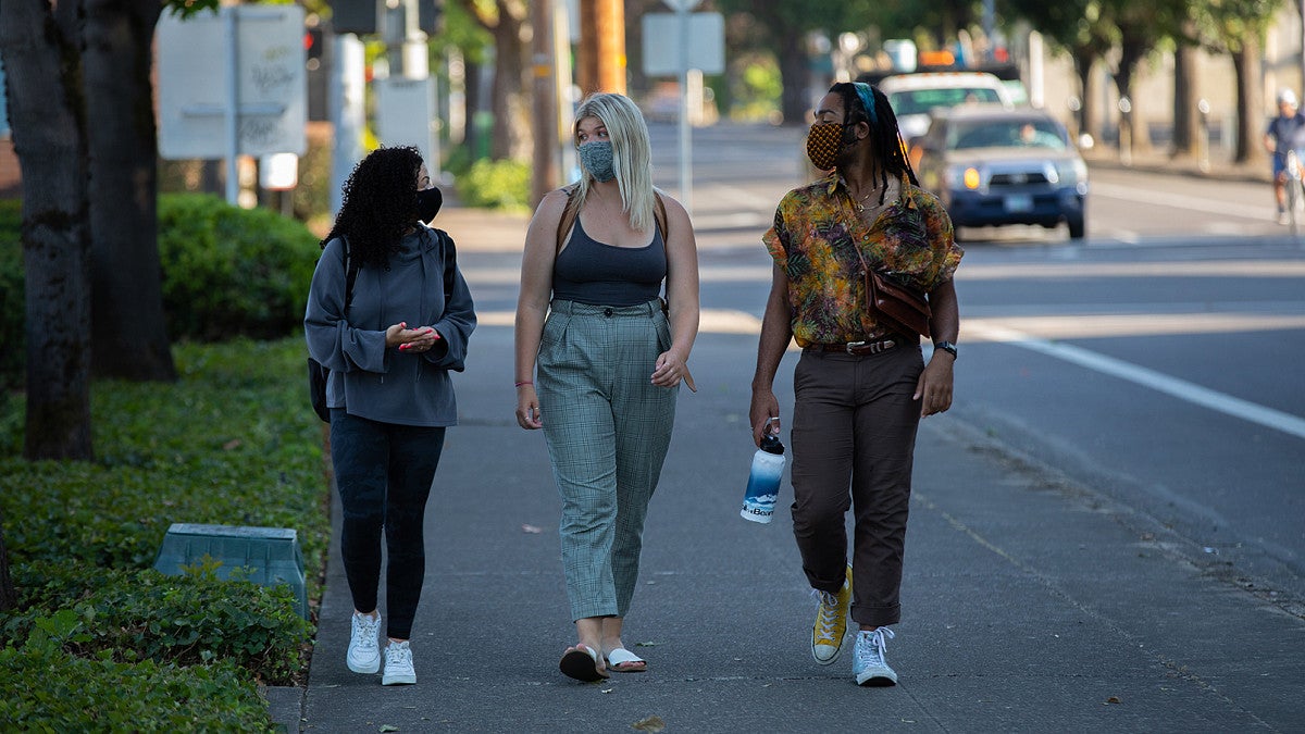 three students wearing face masks and walking on sidewalk