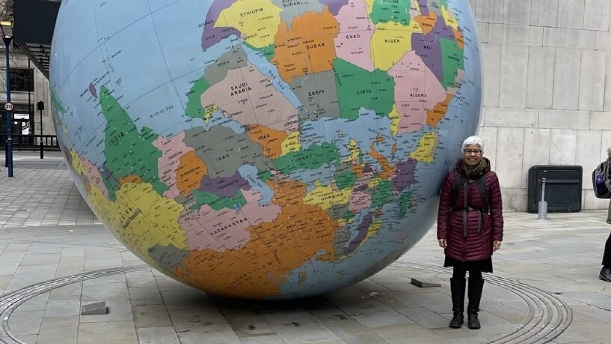Faculty member Laura Pulido standing next to a giant globe