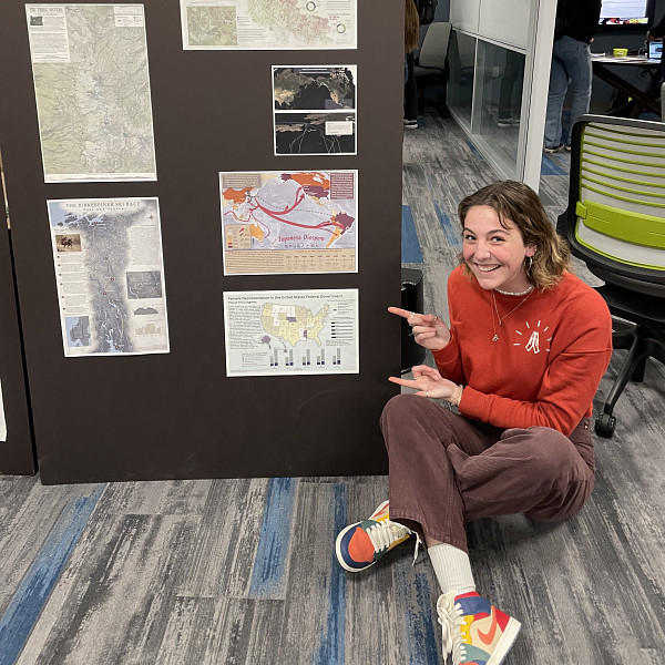 Abby Whelan sitting on the floor pointing at maps on a board