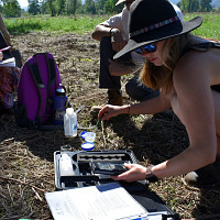 A person crouched over a testing kit and paper in a grassy field. 